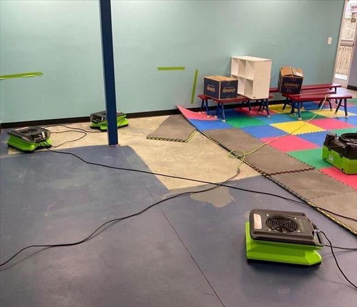 Preschool gym with partially removed puzzle floor tiles and multiple air movers