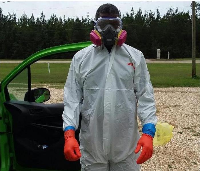 SERVPRO tech, donned in PPE, standing beside vehicle's open door