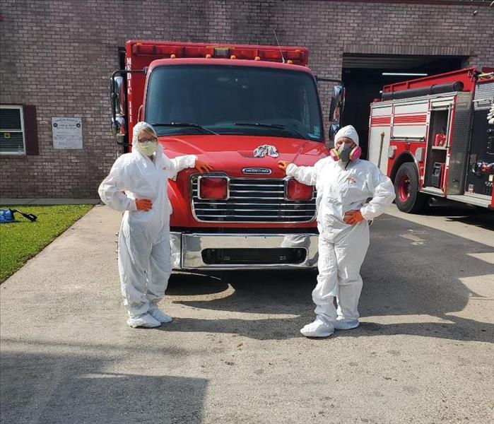 two employees posing in white Tyvek suits in from of a fire truck