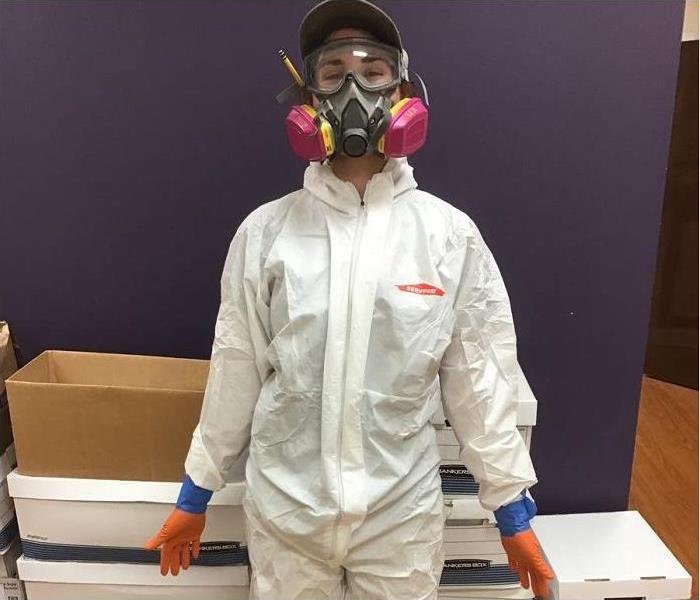 SERVPRO tech, donned in PPE standing in hallway of office; boxes in background