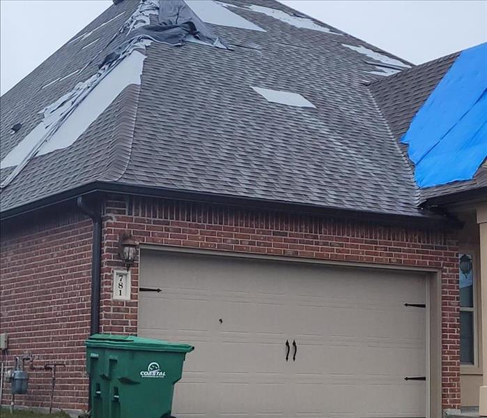 Heavily damaged home roof exterior with damaged shingles, flashing, and partial tarping