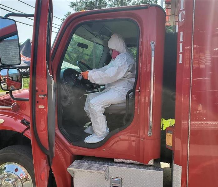 worker, dressed in white Tyvek suit is cleaning a steering wheel in an ambulance