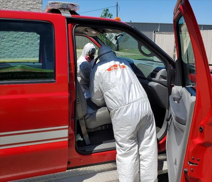 two SERVPRO employees in white protective suits cleaning a red vehicle