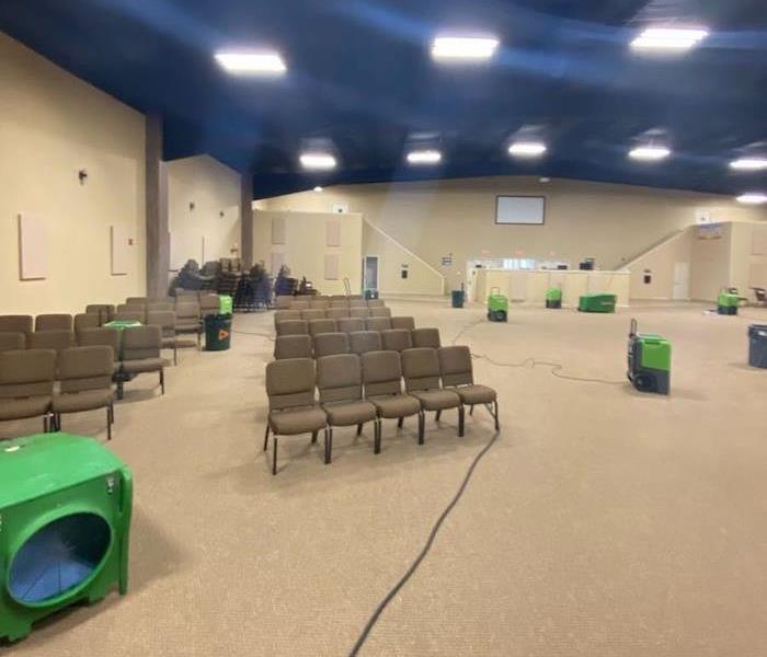 Large commercial room with SERVPRO drying equipment by stacked chairs
